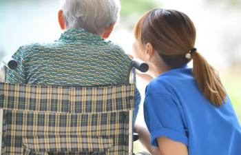 Pflegekraft spricht f&uuml;rsorglich mit einem &auml;lteren Patienten im Rollstuhl